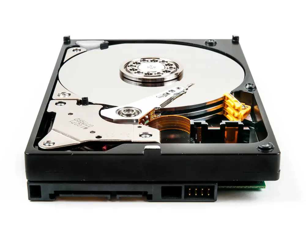 Hard drive with its cover removed on a white surface, showing the shiny platter and the read arm