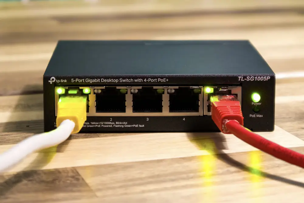 Small black desktop network switch on a wooden surface with yellow and red Ethernet cables plugged in